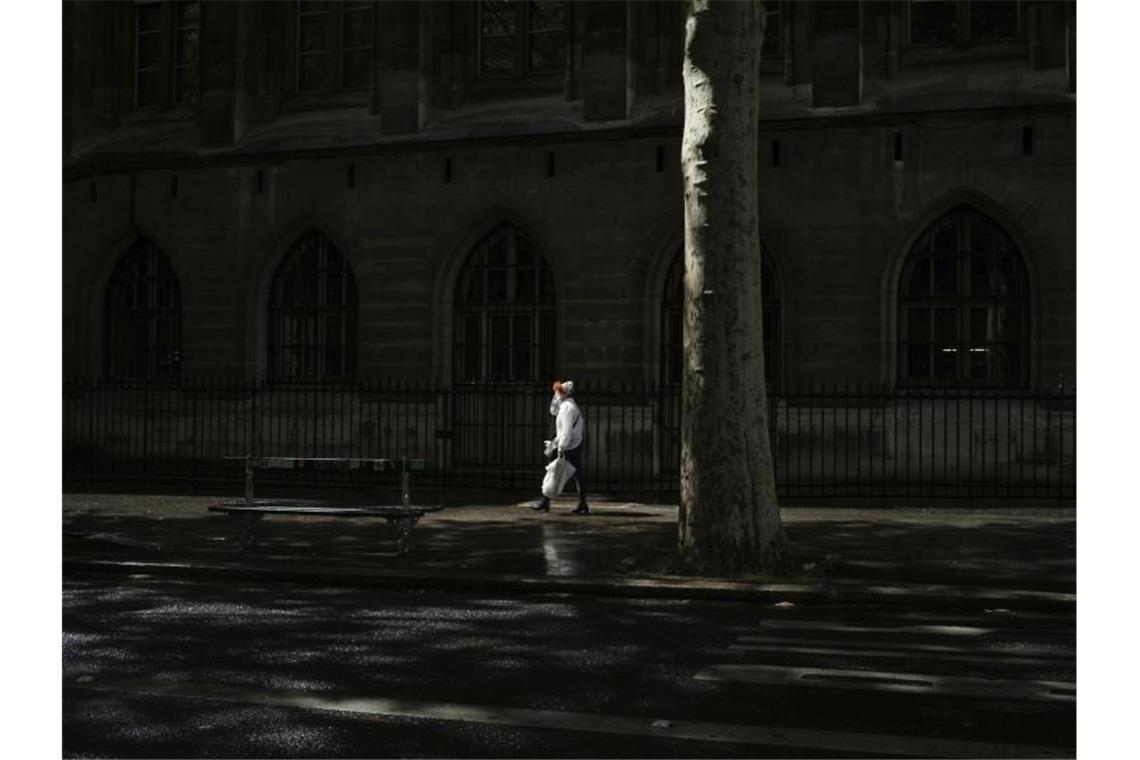 Eine Frau mit Mundschutz geht eine Straße in Paris entlang. Foto: Thibault Camus/AP/dpa