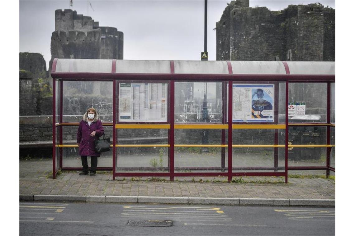 Britische Regierung schließt nationalen Lockdown nicht aus Eine Frau mit Mundschutz wartet in Caerphilly an einer Haltestelle auf den Bus. Großbritannien droht ein erneuter landesweiter Lockdown. Foto: Ben Birchall/PA/AP/dpa