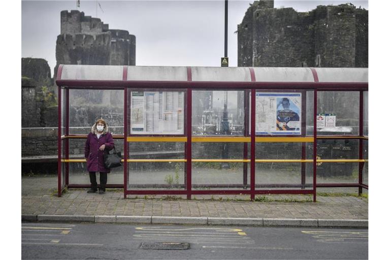 Eine Frau mit Mundschutz wartet in Caerphilly an einer Haltestelle auf den Bus. Großbritannien droht ein erneuter landesweiter Lockdown. Foto: Ben Birchall/PA/AP/dpa