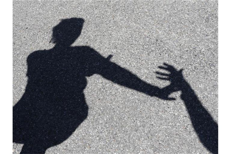 Eine Frau, nach der ein Mann greift, beide im Schattenriss. Foto: Karl-Josef Hildenbrand/dpa/Symbolbild