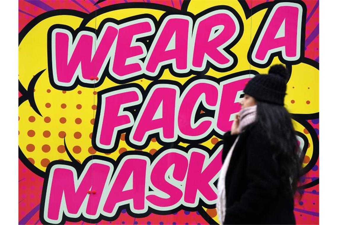 Eine Frau ohne Mund-Nasen-Schutz geht an einem farbigen Schild in Nottingham vorbei, das zum Tragen einer Mund-Nasen-Bedeckung auffordert. Foto: Zac Goodwin/PA Wire/dpa