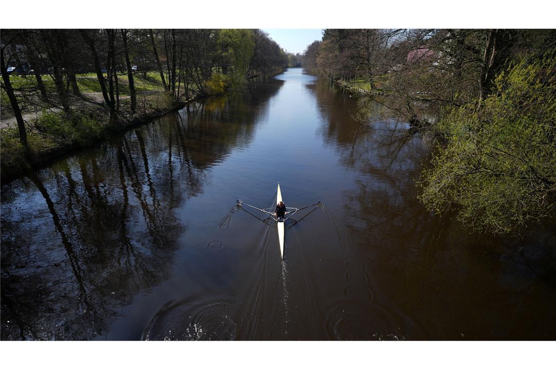 Eine Frau rudert mit ihrem Kajak bei schönstem Sonnenschein auf der Alster in Richtung Außenalster.