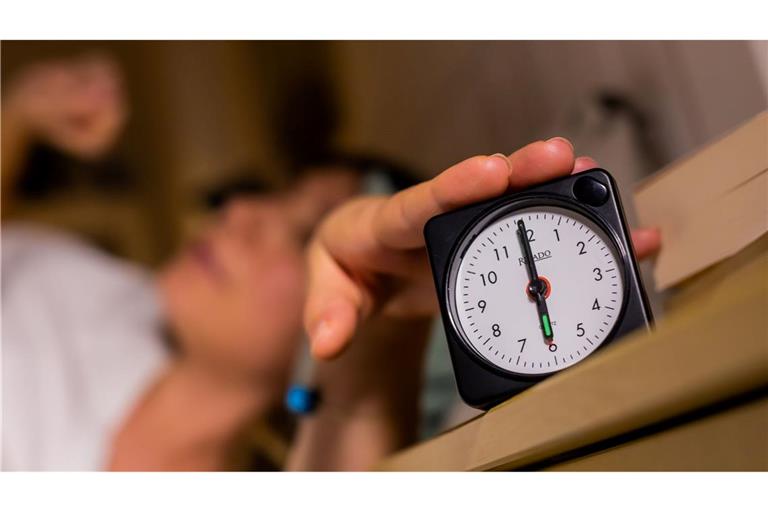 Eine Frau schaltet vom Bett aus einen auf sechs Uhr gestellten Wecker aus.