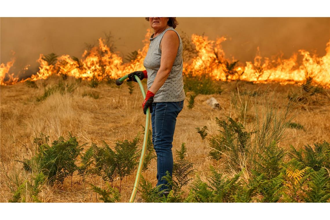 Eine Frau schaut erschöpft, als sie versucht, mit einem Schlauch gegen die Ausbreitung eines Feuers in Santa Baia De Montes in Spanien anzukämpfen.