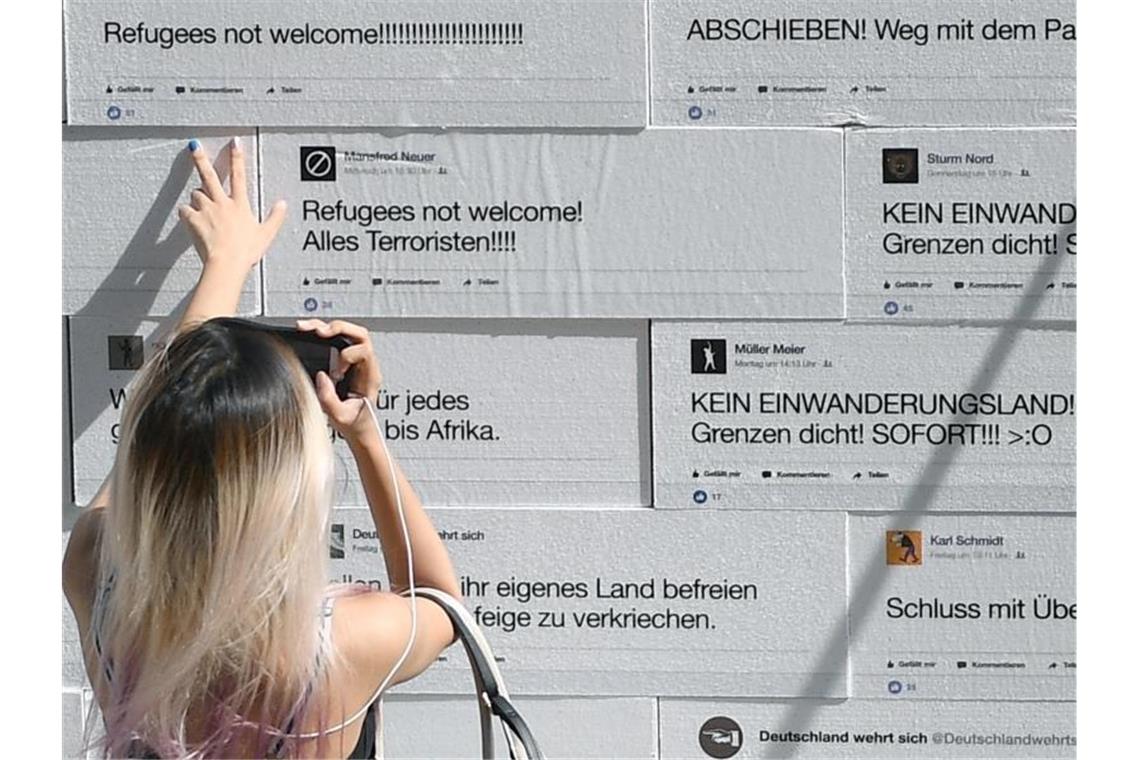 Neun Punkte gegen den Hass Eine Frau schaut sich auf dem Berliner Gendarmenmarkt eine Mauer an, auf die sogenannte „hate speech“ gedruckt ist. Die Mauer voller Hass-Botschaften wurde symbolisch zum Einsturz gebracht. Foto: Britta Pedersen/zb/dpa