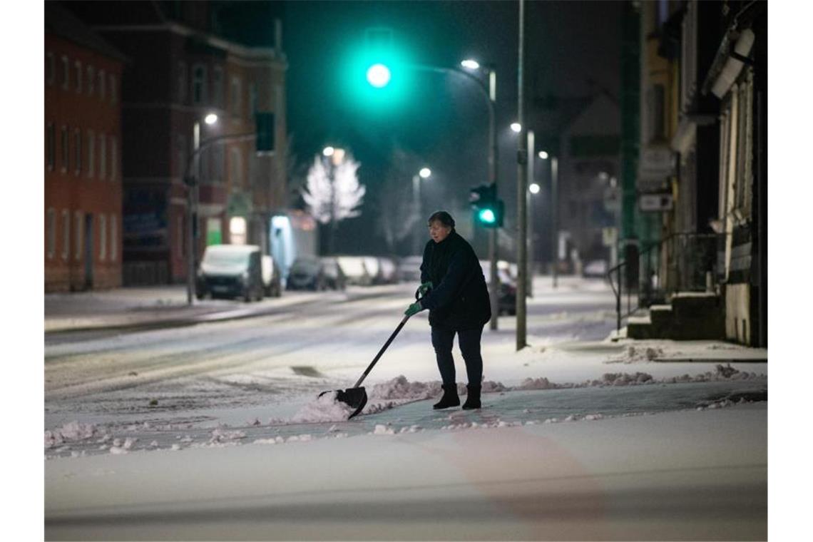 Eine Frau schippt am frühen Morgen Schnee auf einem Bürgersteig in Gevelsberg. Foto: Jonas Güttler/dpa