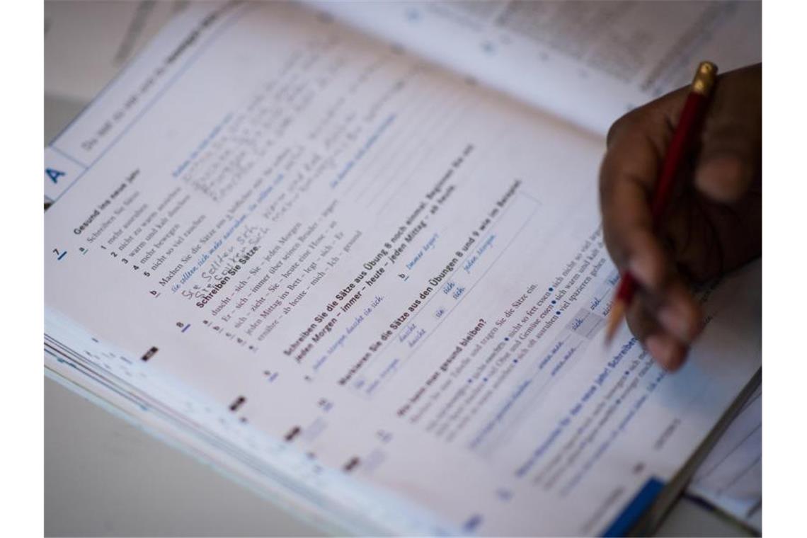 Verpflichtete Teilnehmer warten Monate auf Integrationskurse Eine Frau schreibt in ein Lehrbuch eines Integrationskurses. Foto: Sophia Kembowski/Archiv