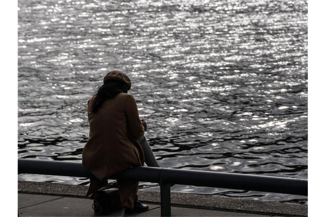 Eine Frau sitzt allein an einem Flussufer. Foto: Paul Zinken/dpa/ZB/Archivbild/Symbolbild