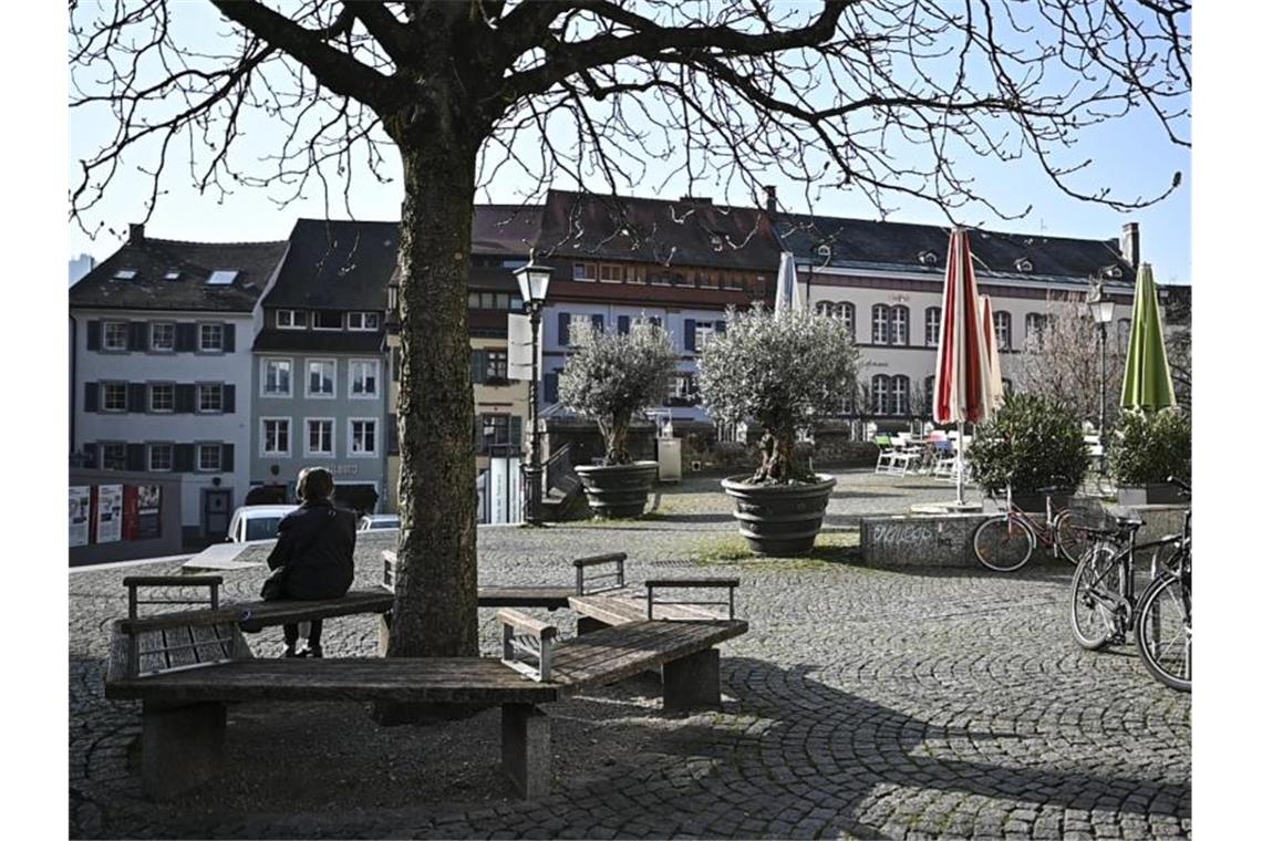 Eine Frau sitzt am leeren Augustinerplatz unter einem Baum. Foto: Patrick Seeger/dpa