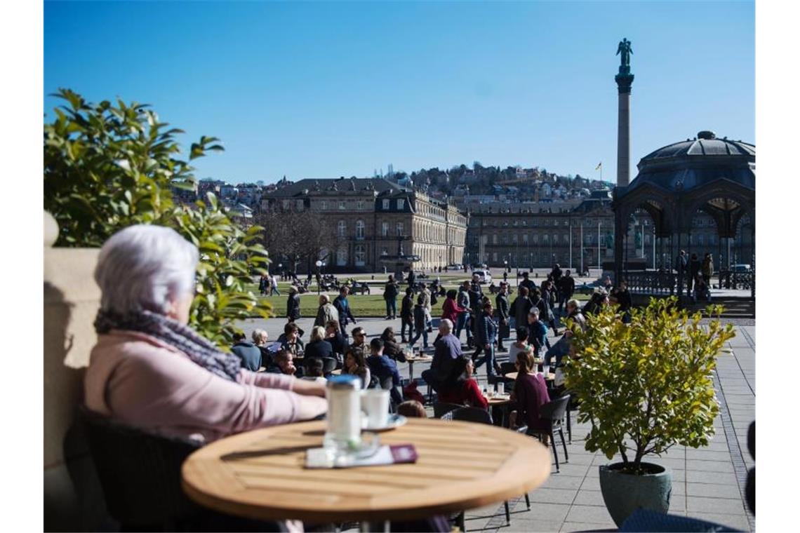 Eine Frau sitzt an einem sonnigen Tag in einem Café am Schlossplatz. Foto: picture alliance/Lino Mirgeler/dpa/Archivbild