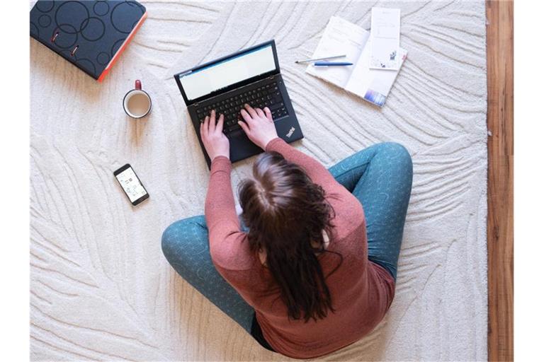 Eine Frau sitzt im Homeoffice auf einem Teppich und arbeitet an einem Laptop. Foto: Sebastian Kahnert/dpa-Zentralbild/dpa/Illustration
