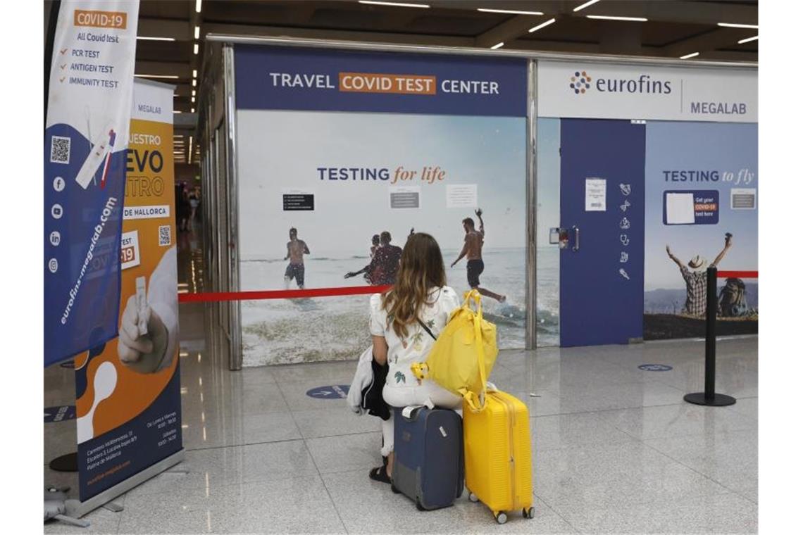 Eine Frau sitzt vor dem Testzentrum am Flughafen von Palma de Mallorca auf Koffern. Foto: Clara Margais/dpa