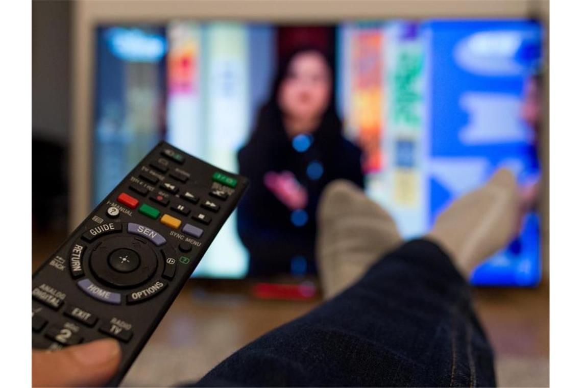 Eine Frau sitzt vor einem Fernseher und hält eine Fernbedienung in der Hand. Foto: Monika Skolimowska/dpa/Archivbild