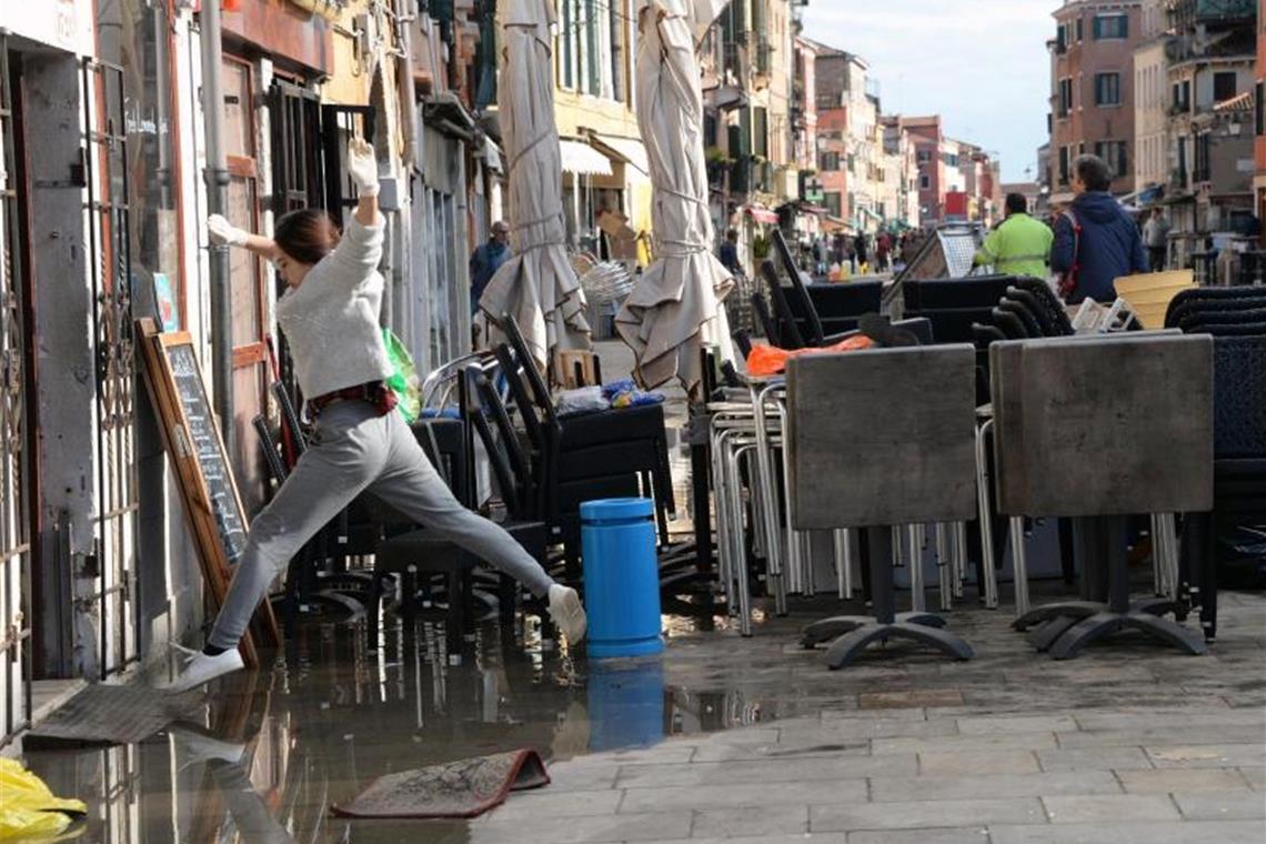 Eine Frau springt während der Reinigung nach dem Hochwasser über eine Pfütze. Foto: Andrea Merola/ANSA/dpa