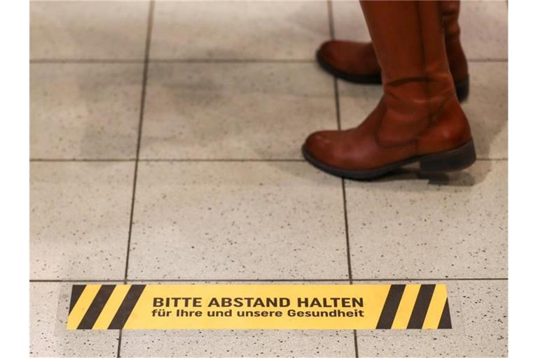 Eine Frau steht an der Kasse eines Supermarkt hinter einem Warnaufkleber, der um Abstand bitte. Foto: Jan Woitas/dpa-Zentralbild/dpa/Symbolbild