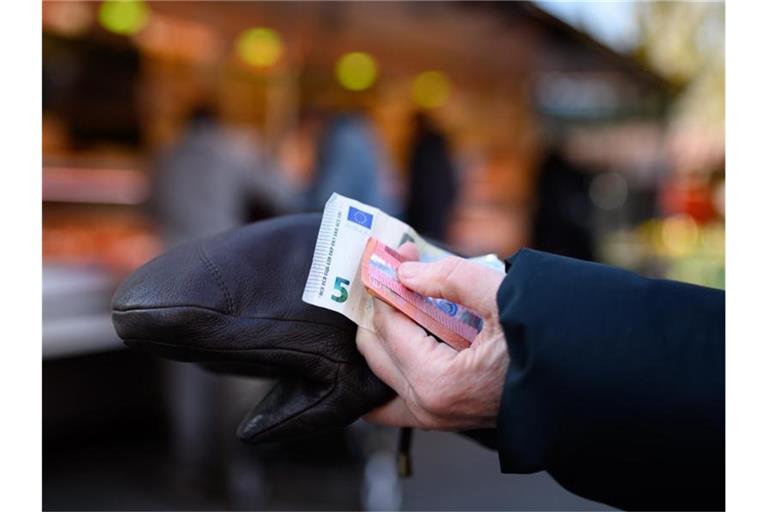 Eine Frau steht an einem Marktstand und hält das Bargeld für ihren Einkauf bereit. Foto: Jonas Walzberg/dpa