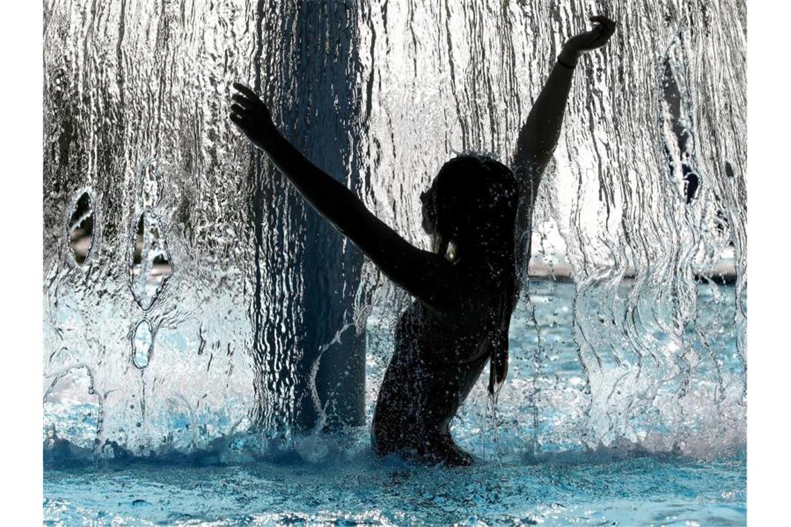 Eine Frau steht im Freibad unter einem Wasserpilz und erfrischt sich. Foto: Thomas Warnack/dpa/Archivbild