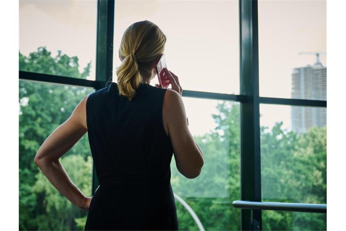 Eine Frau steht in einem Büro am Fenster und telefoniert. Foto: Annette Riedl/dpa/Illustration