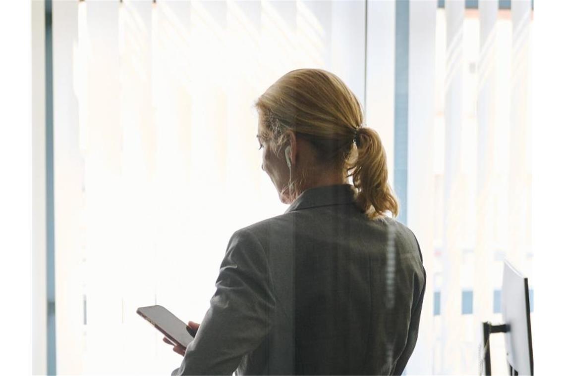 Eine Frau steht in einem Bürozimmer und hält ein Smartphone in der Hand. (Symbolbild). Foto: Annette Riedl/dpa