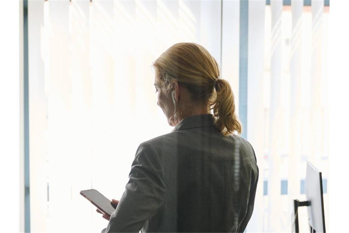 Studie: Weniger Chefinnen in mittelständischen Firmen Eine Frau steht in einem Bürozimmer und hält ein Smartphone in der Hand (gestellte Szene). Foto: Annette Riedl/dpa