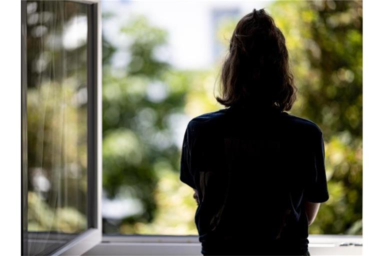 Eine Frau steht in ihrer Wohnung an einem Fenster. (Archivbild). Foto: Fabian Sommer/dpa