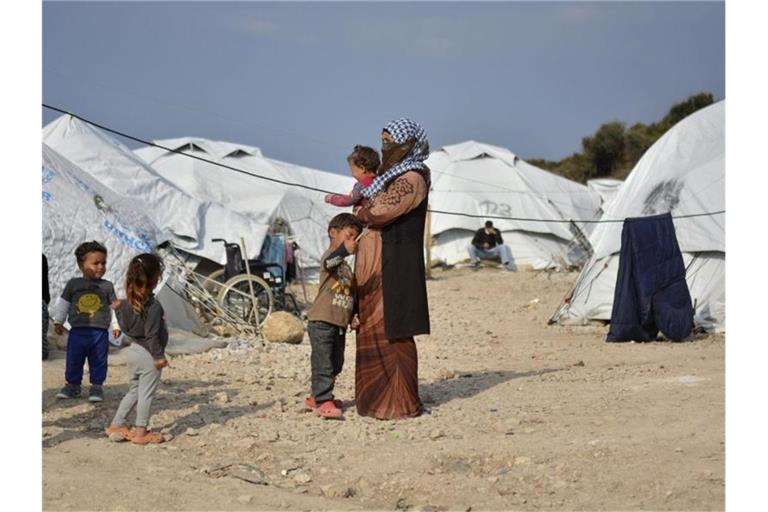 Eine Frau steht mit einem Baby im Arm und drei kleinen Kindern im Flüchtlingslager Kara Tepe in der Nähe von Mytilini auf Lesbos zwischen Zelten. Foto: Panagiotis Balaskas/AP/dpa