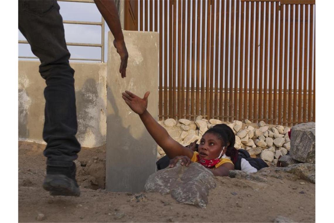 Eine Frau streckt die Hand nach Hilfe aus, während sie aus einem felsigen Kanal neben einer Lücke in der US-Grenzmauer an der mexikanischen Grenze klettert. Foto: Eugene Garcia/AP/dpa