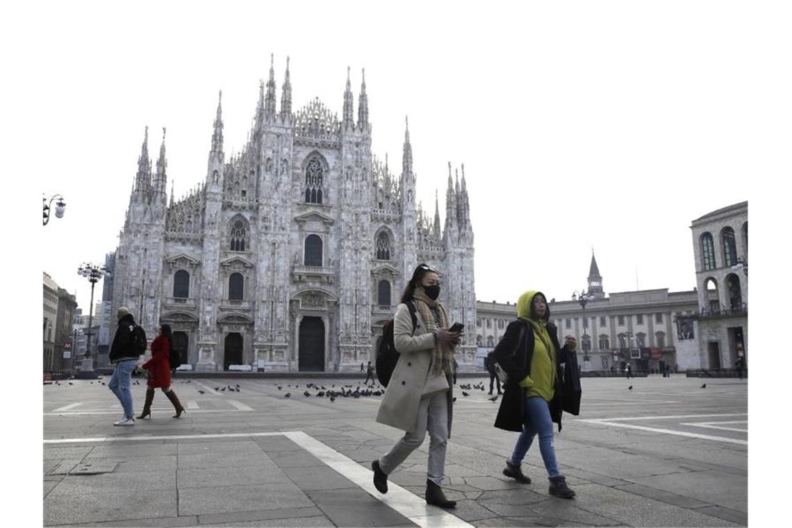 Eine Frau trägt eine Atemschutzmaske und läuft über den fast leeren Platz vor dem Mailänder Dom. Foto: Luca Bruno/AP/dpa/Archivbild