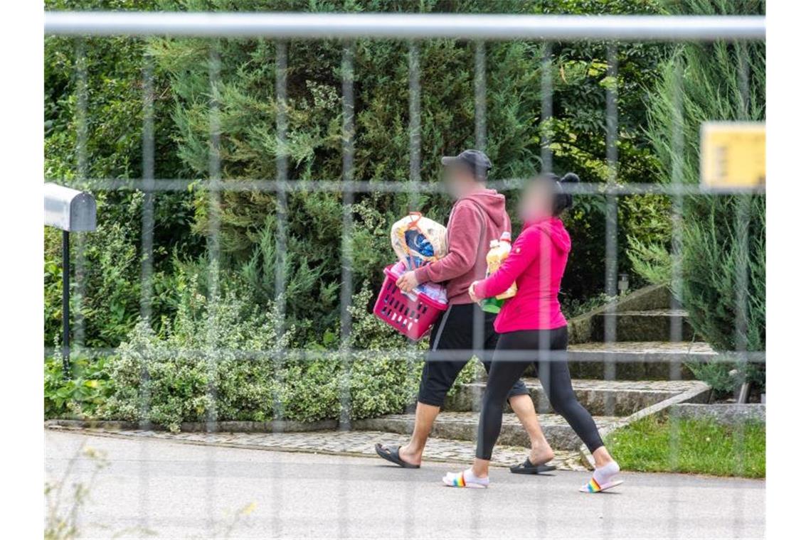 Corona-Ausbruch in Bayern: 174 Erntehelfer angesteckt Eine Frau und ein Mann gehen hinter einem Absperrzaun auf dem Gelände des Hofs. Foto: Armin Weigel/dpa