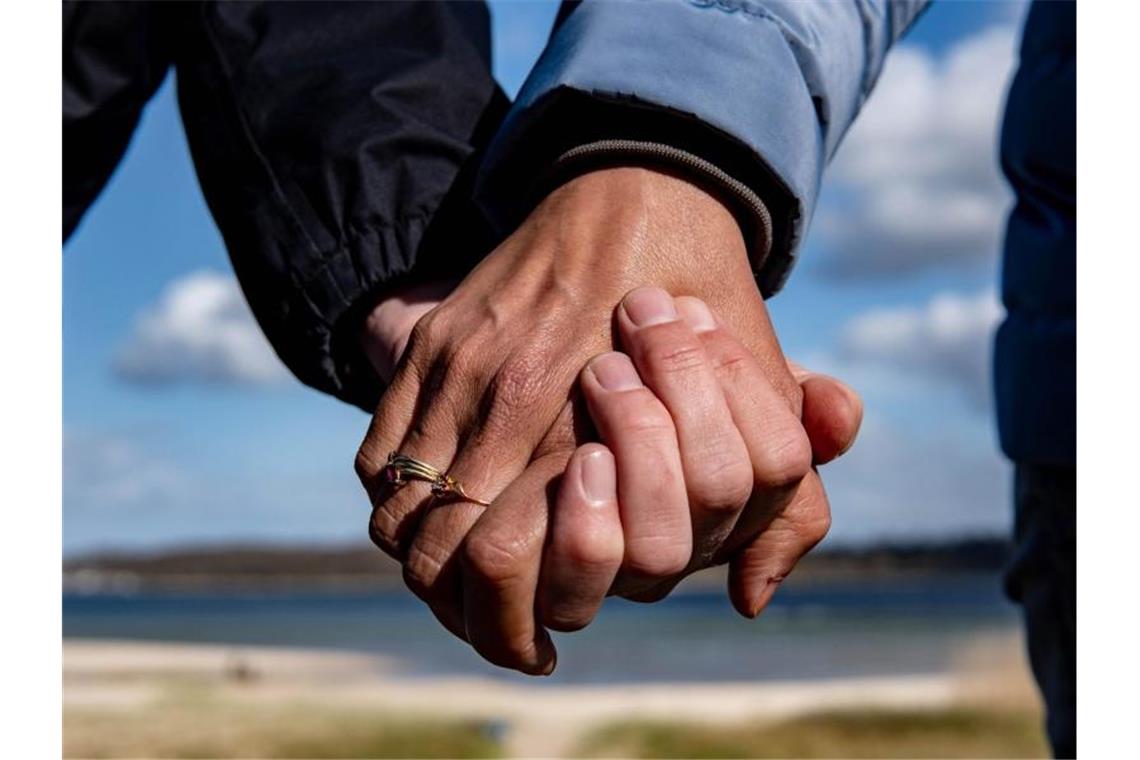 Eine Frau und ein Mann halten sich bei einem Strandspaziergang an den Händen. Foto: Axel Heimken/dpa
