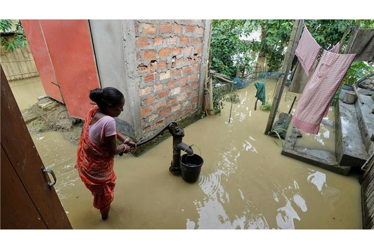 Eine Frau versucht in der überfluteten Umgebung ihres Hauses, Wasser zu sammeln.