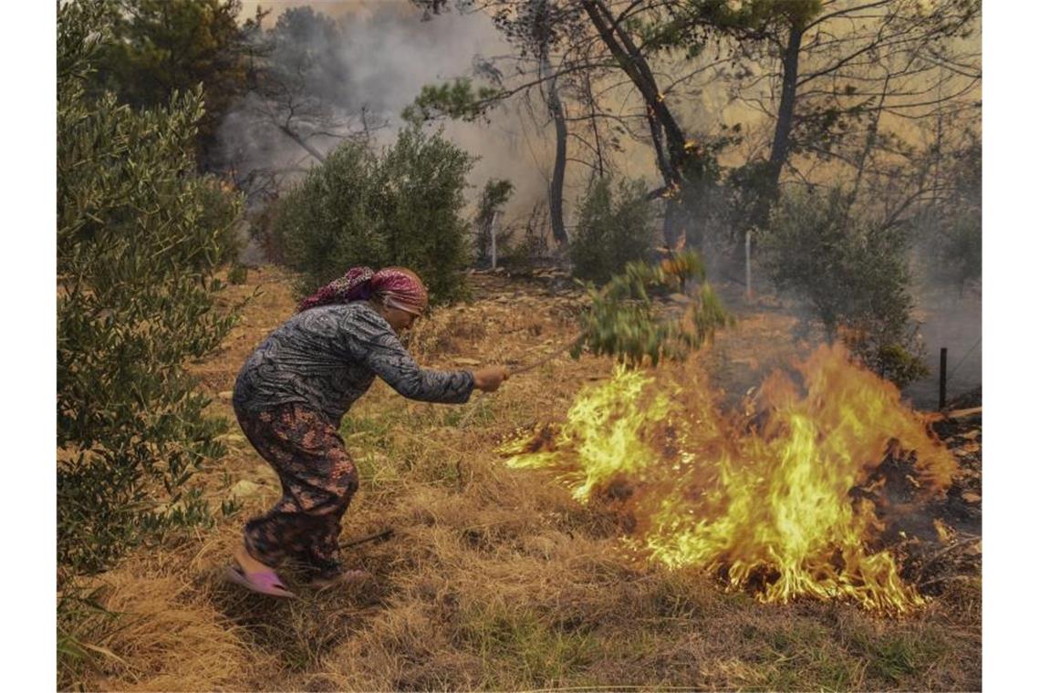 Eine Frau versucht mit einem Zweig ein Feuer auszuschlagen. Nachdem zwei Forstarbeiter bei Löscharbeiten in der südtürkischen Provinz Antalya ums Leben gekommen sind, stieg die Anzahl der Todesopfer auf sechs. Foto: Uncredited/AP/dpa