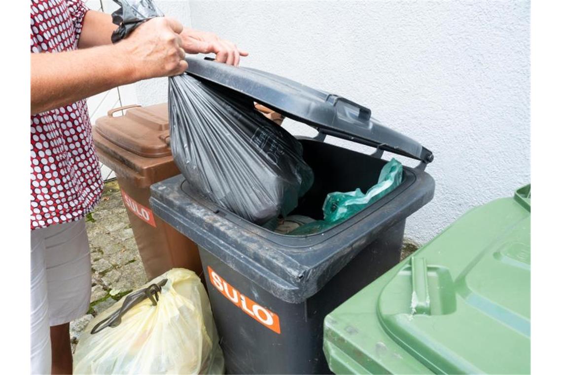 Eine Frau wirft einen Sack mit Restmüll in eine graue Restmülltonne. Foto: Bernd Weißbrod/dpa