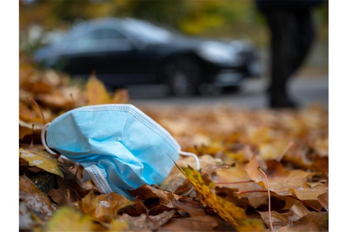 Eine Gesichtsmaske liegt am Straßennrand im Herbstlaub. Foto: Sebastian Gollnow/dpa/Archivbild