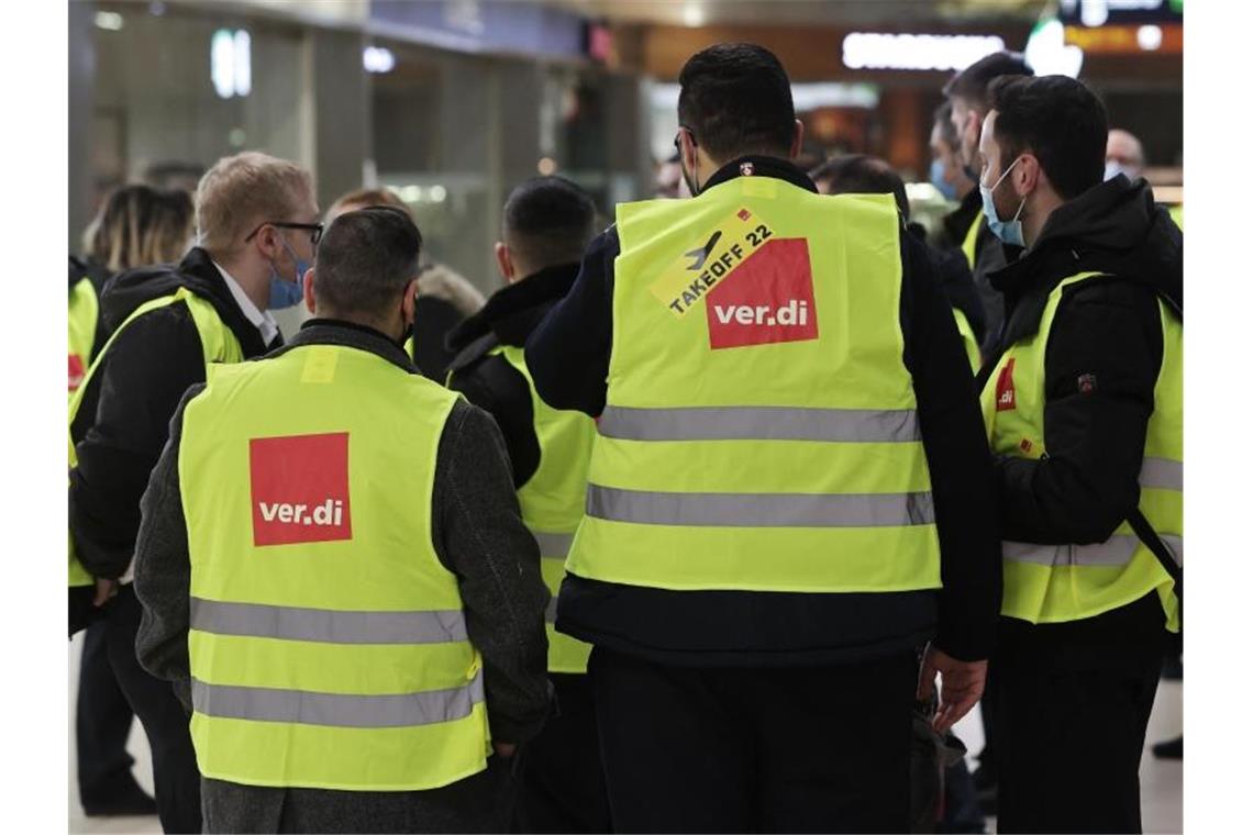 Verdi ruft für Montag zu Warnstreiks an Flughäfen auf Eine Gruppe Streikender mit gelben Verdi-Westen versammelt sich im Köln-Bonn-Airport (Februar). Foto: David Young/dpa