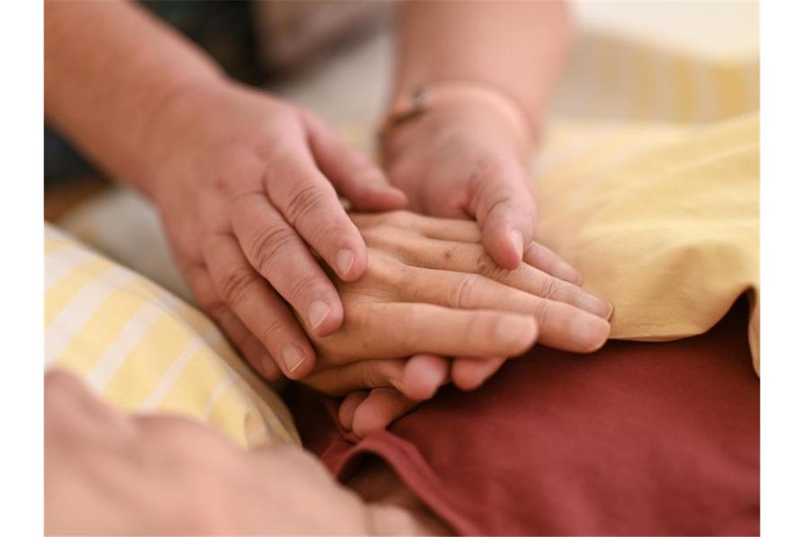 Pflege: SPD fordert 2500 zusätzliche Plätze Eine Hospizmitarbeiterin hält die Hand eines Patienten, der im Bett liegt. Foto: Felix Kästle/dpa