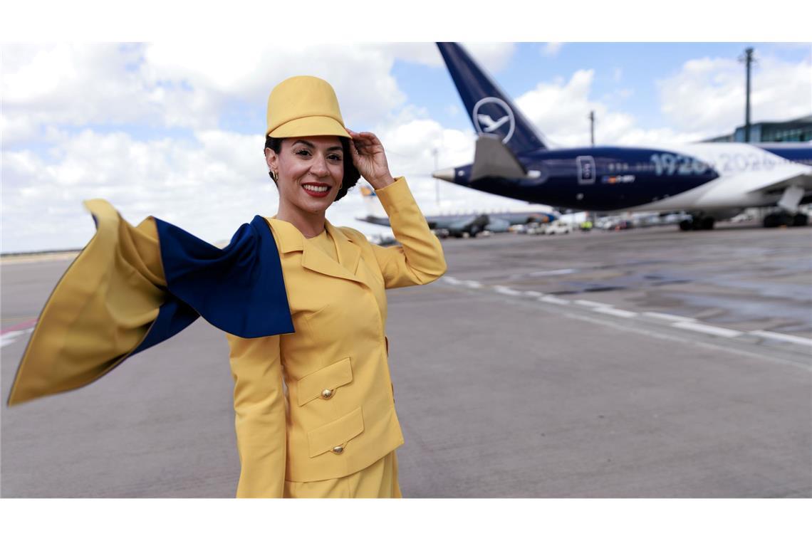 Eine Hostess trägt eine frühere Lufthansa-Uniform vor einem Passagierflugzeug der Lufthansa auf dem Flughafen Berlin-Brandenburg (BER) bei der Feier von Lufthansa zum 100. Jahrestag des Erstflugs.
