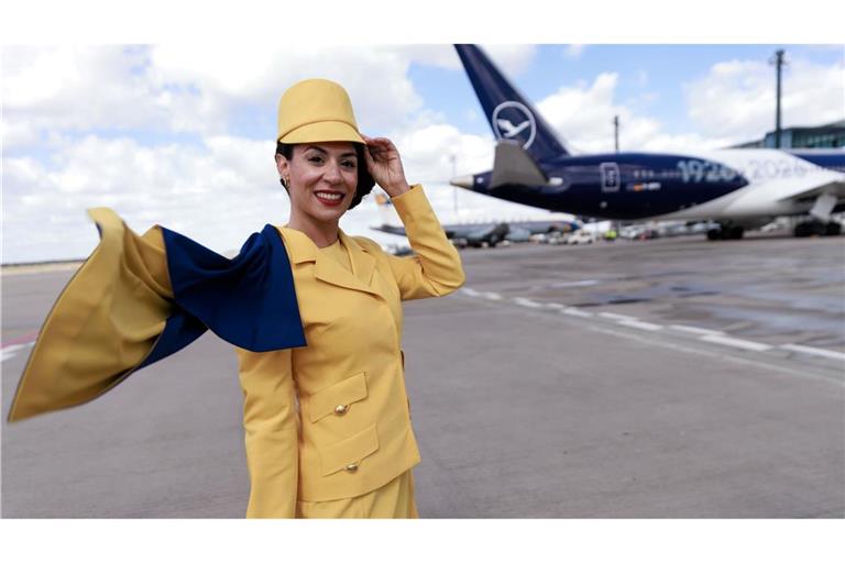 Eine Hostess trägt eine frühere Lufthansa-Uniform vor einem Passagierflugzeug der Lufthansa auf dem Flughafen Berlin-Brandenburg (BER) bei der Feier von Lufthansa zum 100. Jahrestag des Erstflugs.
