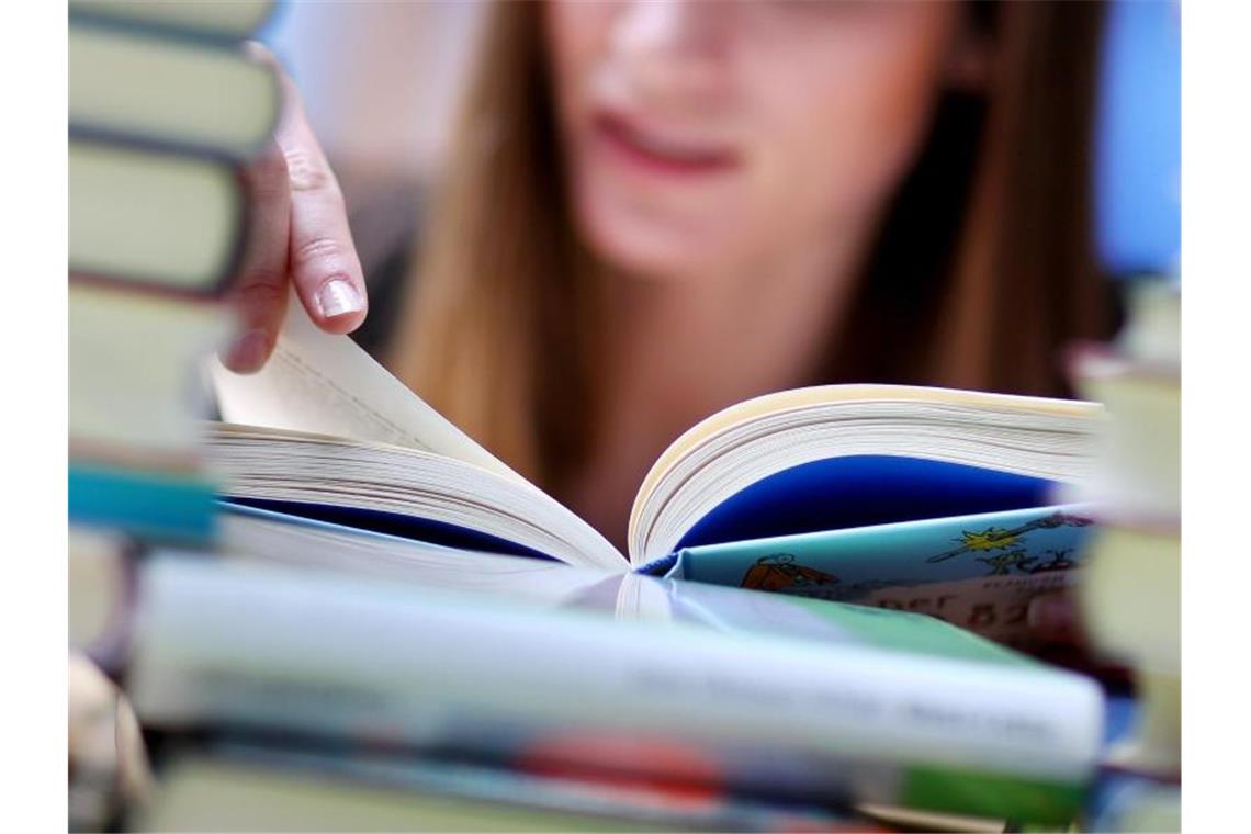 Abholservice jetzt an allen Bibliotheken erlaubt Eine junge Frau liest an einem Tisch voller Bücher. Foto: Jan Woitas/dpa-Zentralbild/dpa/Illustration