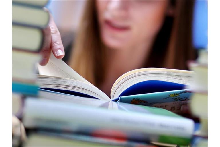 Eine junge Frau liest an einem Tisch voller Bücher. Foto: Jan Woitas/dpa-Zentralbild/dpa/Illustration