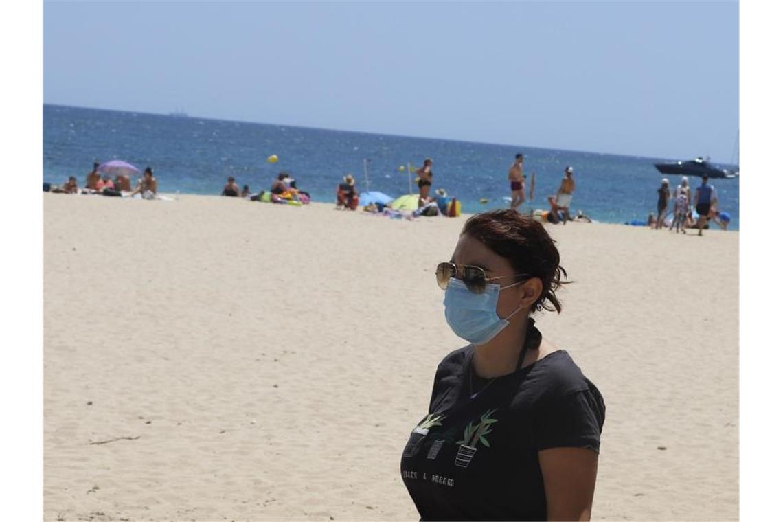 Eine junge Frau mit einer Schutzmaske an einem Strand. Foto: Clara Margais/dpa