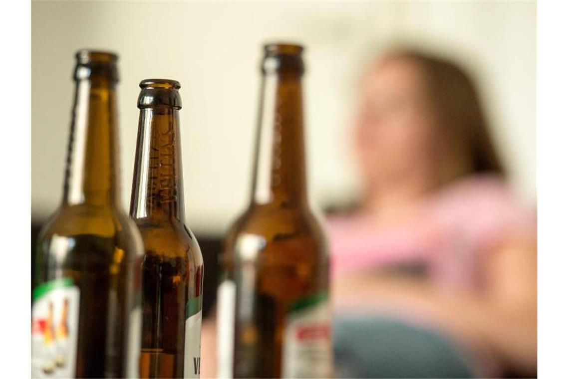 Eine junge Frau sitzt hinter leeren Bierflaschen. Foto: Alexander Heinl/Archivbild