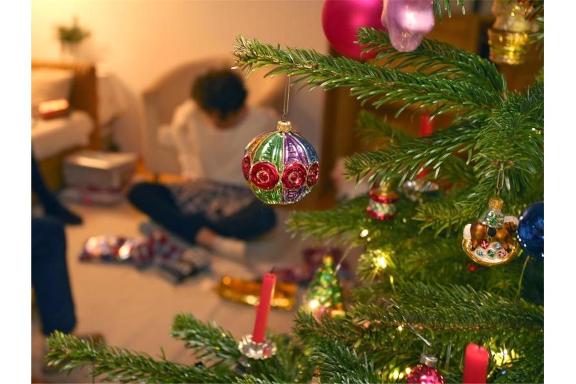 Eine Junge packt hinter einem geschmücktem Christbaum Weihnachtsgeschenke aus. Foto: Karl-Josef Hildenbrand/dpa