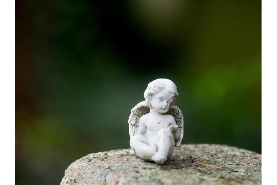 Eine kleine Engelsfigur hockt auf einem Grabstein auf dem Stadtfriedhof. Foto: Julian Stratenschulte/Archivbild