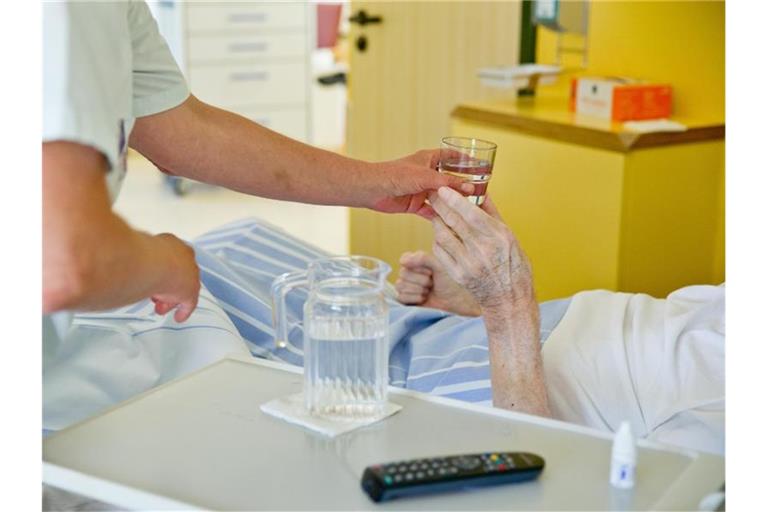 Eine Krankenpflegerin reicht einem Patienten in einem Klinikum ein Glas Wasser. Foto: Daniel Karmann