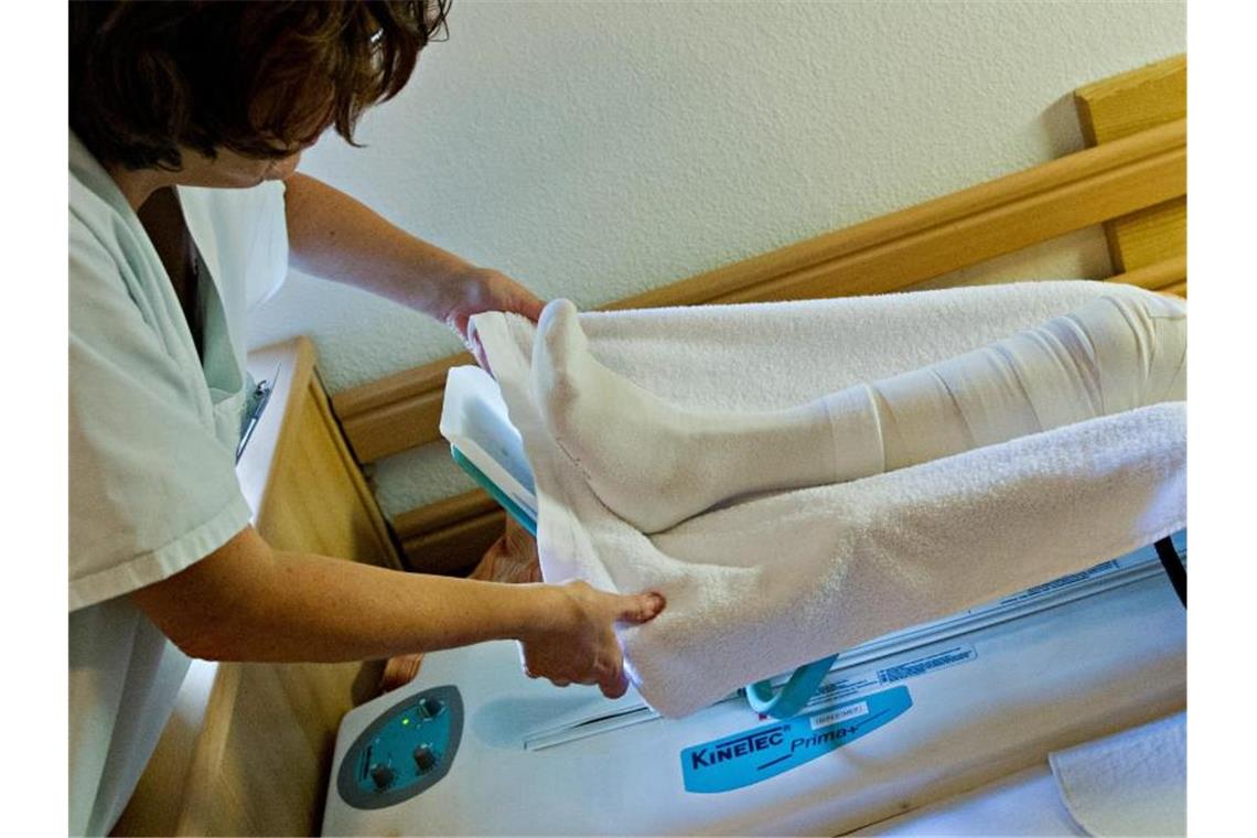 Diakonie Württemberg will Bonuszahlung für Pflegekräfte Eine Krankenschwester hilft in einer Krankenwohnung einer Bewohnerin, ihr Bein in eine Stütze zu heben. Foto: Daniel Bockwoldt/dpa/Archivbild