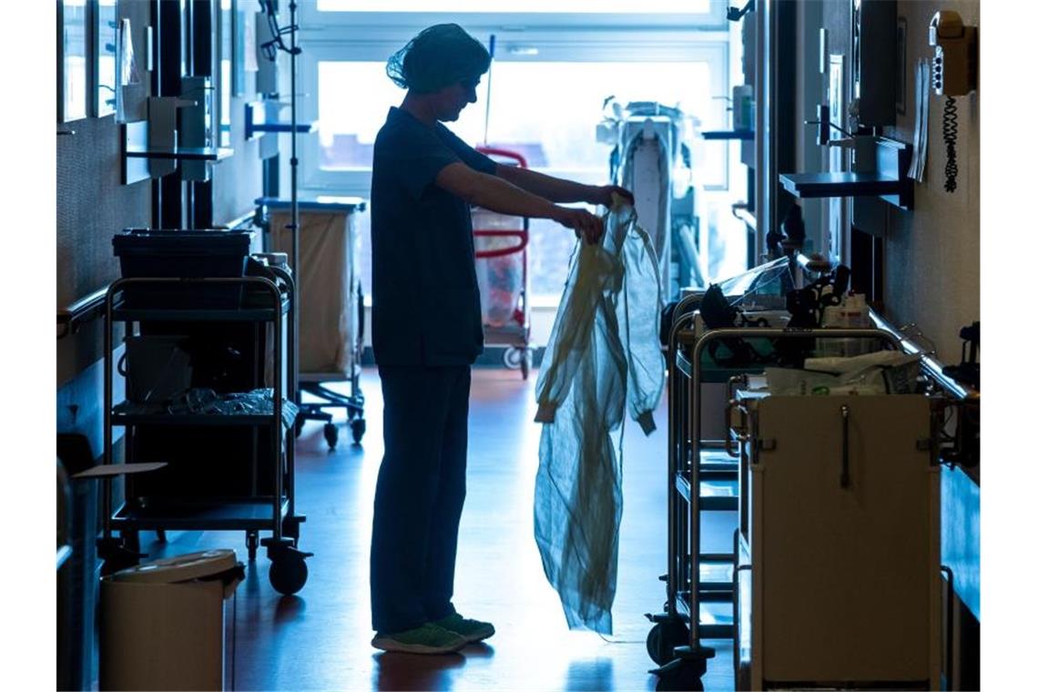Kliniken rechnen noch für Monate mit Corona-Krisenbetrieb Eine Krankenschwester legt auf einer Corona-Isolierstation Schutzkleidung an. Foto: Jens Büttner/dpa-Zentralbild/dpa