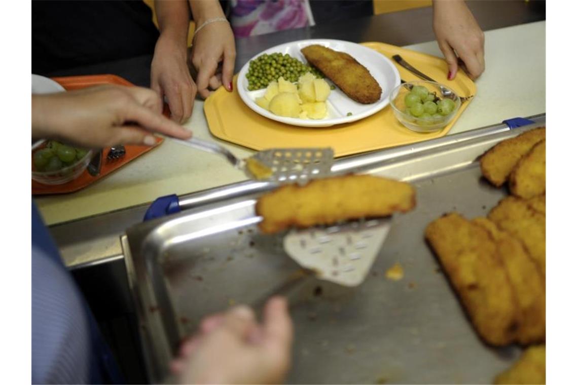 Eine Küchenhelferin legt an einer Gesamtschule ein Stück Fisch auf den Teller eines Schülers. Foto: Alexander Körner/dpa