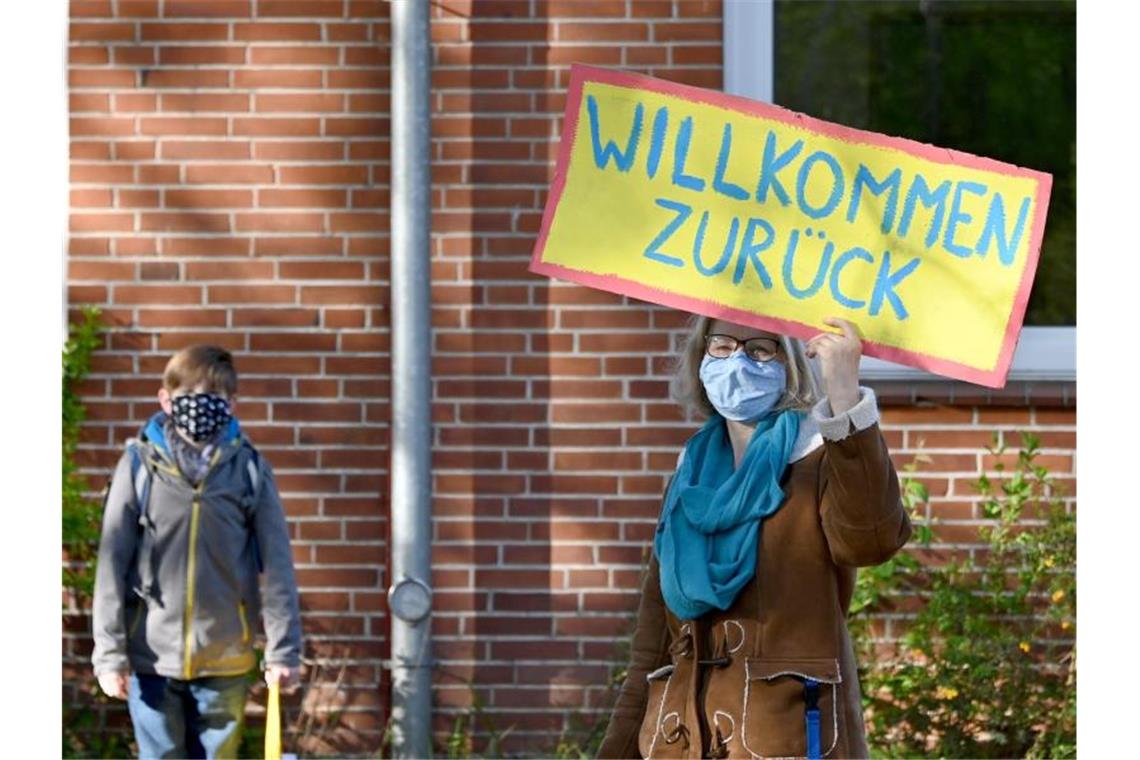 Eine Lehrerin in Schleswig-Holstein begrüßt ihre Schüler mit einem "Willkommen zurück"-Schild. Foto: Carsten Rehder/dpa