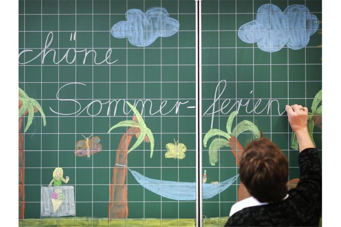 Eine Lehrerin schreibt „Schöne Sommerferien“ an eine Tafel. Foto: picture alliance/Ina Fassbender/dpa/Archiv/Illustration